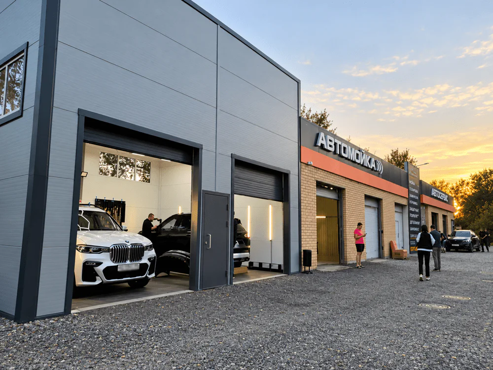 Автотехкомплекс Drive Motors на закате: открытые ворота боксов, вывески «Автомойка» и «Автосервис»